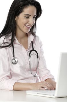 Beautiful young doctor sat smiling at her work desk using her computer.