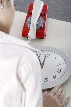 Woman watching the minutes pass on a clock at her desk waiting.