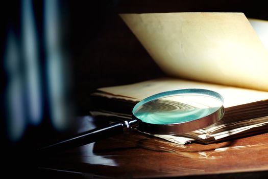 Old book and magnifier glass on a dark background as a symbol of knowledge and science