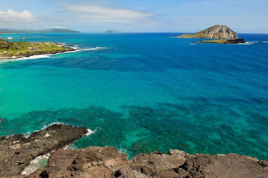 A horizontal shot of the blue and green water off the north coast of the island of Oahu in Hawaii showing several small islands