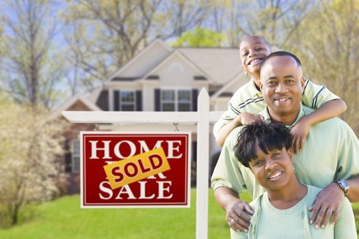 Happy African American Family In Front of Sold Real Estate Sign and House.