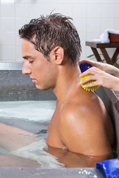 Side view of young man in pool receiving back massage with stress ball by a female