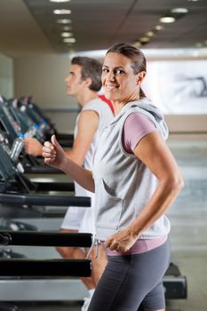 Side view of happy mature woman and man running on treadmill in health club