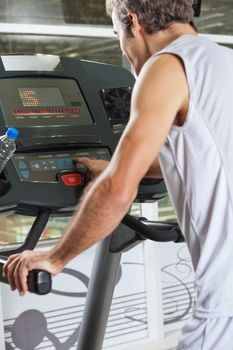 Rear view of young man pressing program button on treadmill in health club