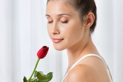 Beautiful calm young woman holding a red rose over white background