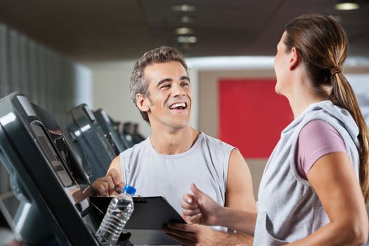 Happy male instructor looking at female client exercising on treadmill in health center