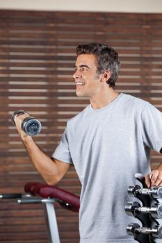 Happy young man lifting dumbbell in health center