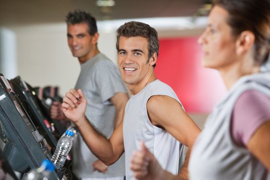 Portrait of happy men and woman running on treadmill in fitness club