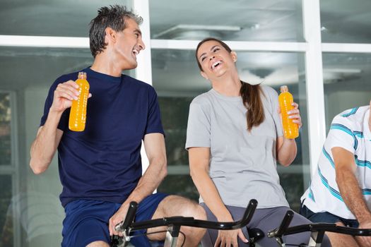 Man and woman holding juice bottles while laughing in health club