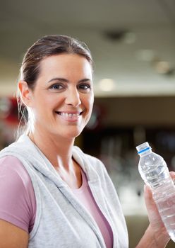 Portrait of happy mature woman holding bottle of water at health club