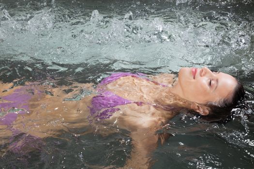 An attractive young woman floating on her back in a Jacuzzi at health spa