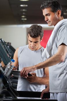 Male instructor making notes on clipboard while standing besides man on treadmill in health club