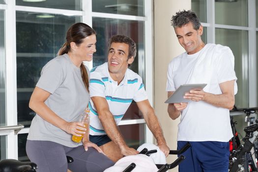 Happy friends using digital tablet while working out in fitness club