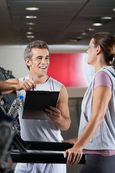 Happy male instructor looking at client exercising on treadmill in health center