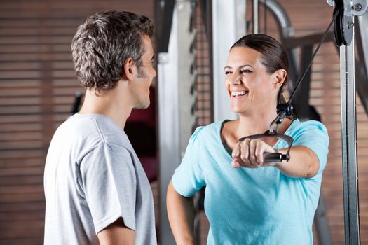 Happy mature woman working out while looking at instructor at health club