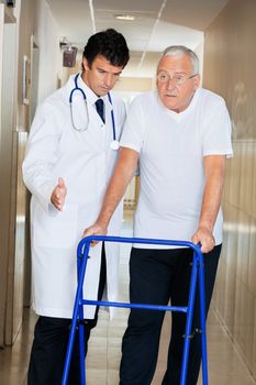 Doctor helping senior patient walk down hallway using Zimmer frame