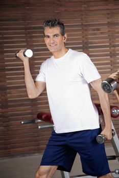 Portrait of happy mature man lifting dumbbells in fitness center