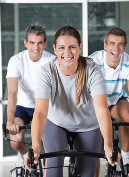 Happy men and woman on exercise bikes in health club