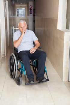 Full length of depressed senior man sitting in a wheelchair at hospital corridor
