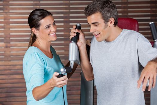 Mature female instructor assisting man in getting down from exercise machine in health club
