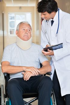 Doctor writing on clipboard while communicating with senior man sitting in wheel chair