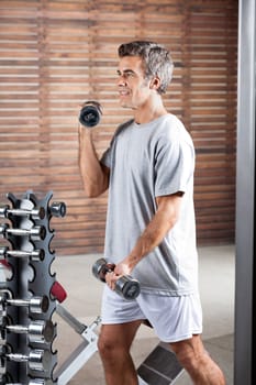 Young man lifting dumbbells in health center