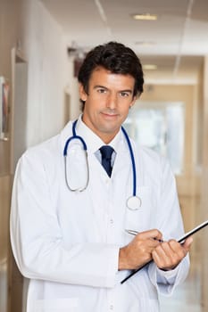 Portrait of young doctor writing report on clipboard