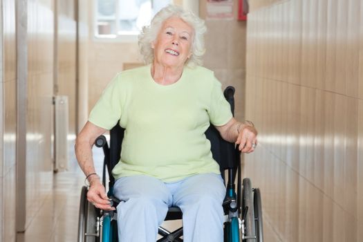 Happy senior woman sitting in a wheel chair at hospital corridor