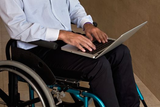 Close-up of man on wheelchair using laptop.