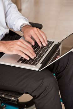Close-up of man on wheelchair using laptop.