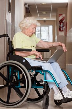 Retired woman on wheelchair using laptop.