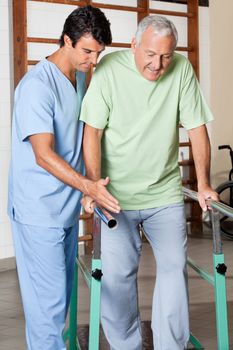 Physical therapist assisting senior man to walk with the support of bars at hospital gym