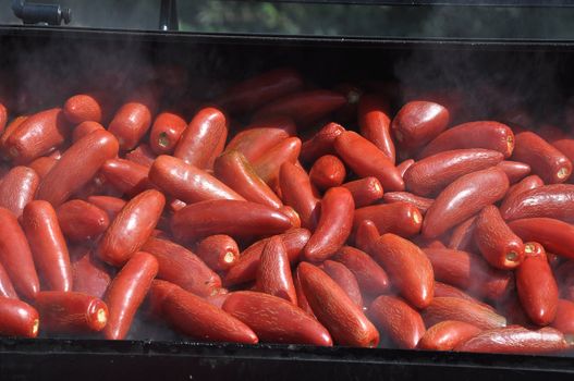 Large batch of hot chili peppers being smoked on a grill