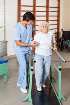 Full length portrait of a physical therapist assisting tired senior woman on walking track at hospital gym