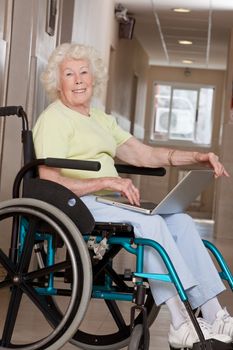 Retired woman on wheelchair using laptop.