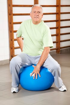 Full length of a senior man sitting on fitness ball at hospital gym