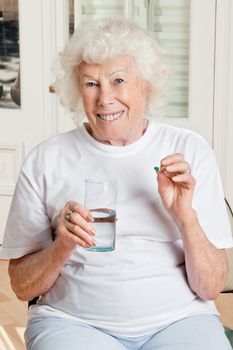 Portrait of a senior woman taking a pill with a glass of water