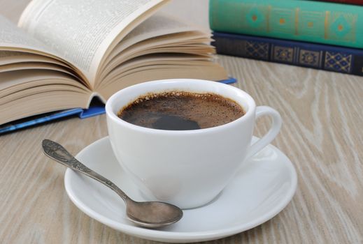A cup of fragrant black coffee on the table against the background of an open book