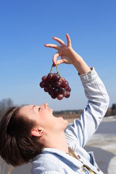 Beautiful young girl handing bunch of red grapes against blue sky background