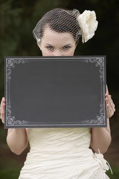 Pretty bride in wedding dress holding a blank board in front of face with space for copy