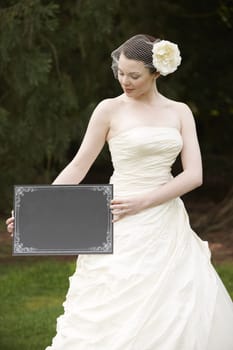 Pretty bride in wedding dress holding a blank board with space for copy