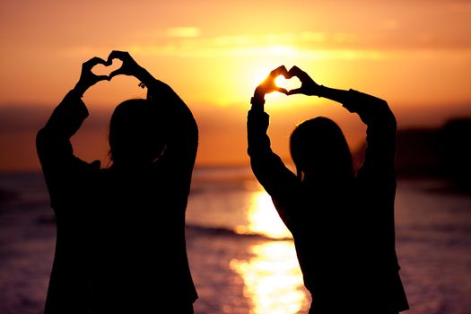 women silhouette makes heart shape sunset