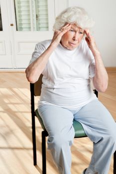 Senior woman sitting on chair suffering from headache