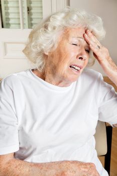 Senior female sitting on chair suffering from headache