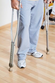 Low section of a woman standing with crutches on a wooden floor