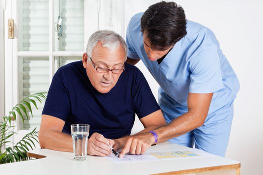 Young male nurse helping senior man in solving puzzle