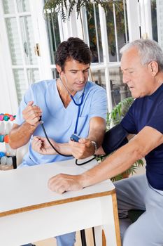 Young male nurse checking blood pressure of a senior patient at hospital