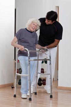 A therapist assisting a senior woman onto her walker.