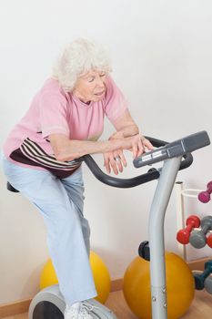 Tired senior woman exercising on bike in gym