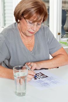 Senior woman playing leisure games with glass of water in foreground